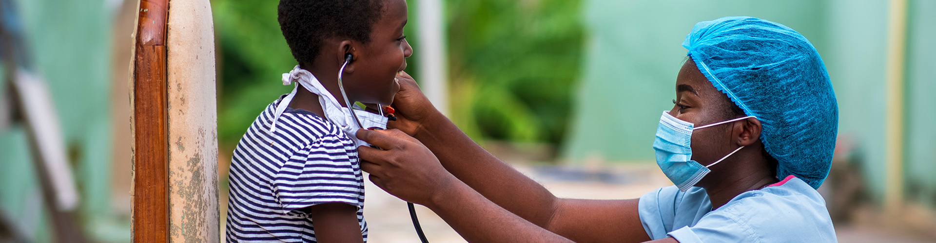 An African doctor pediatrician putting stethoscope in child ear, child cheerfully smiling looking at her; both wearing face mask on face and under chin; Shutterstock ID 1798158742